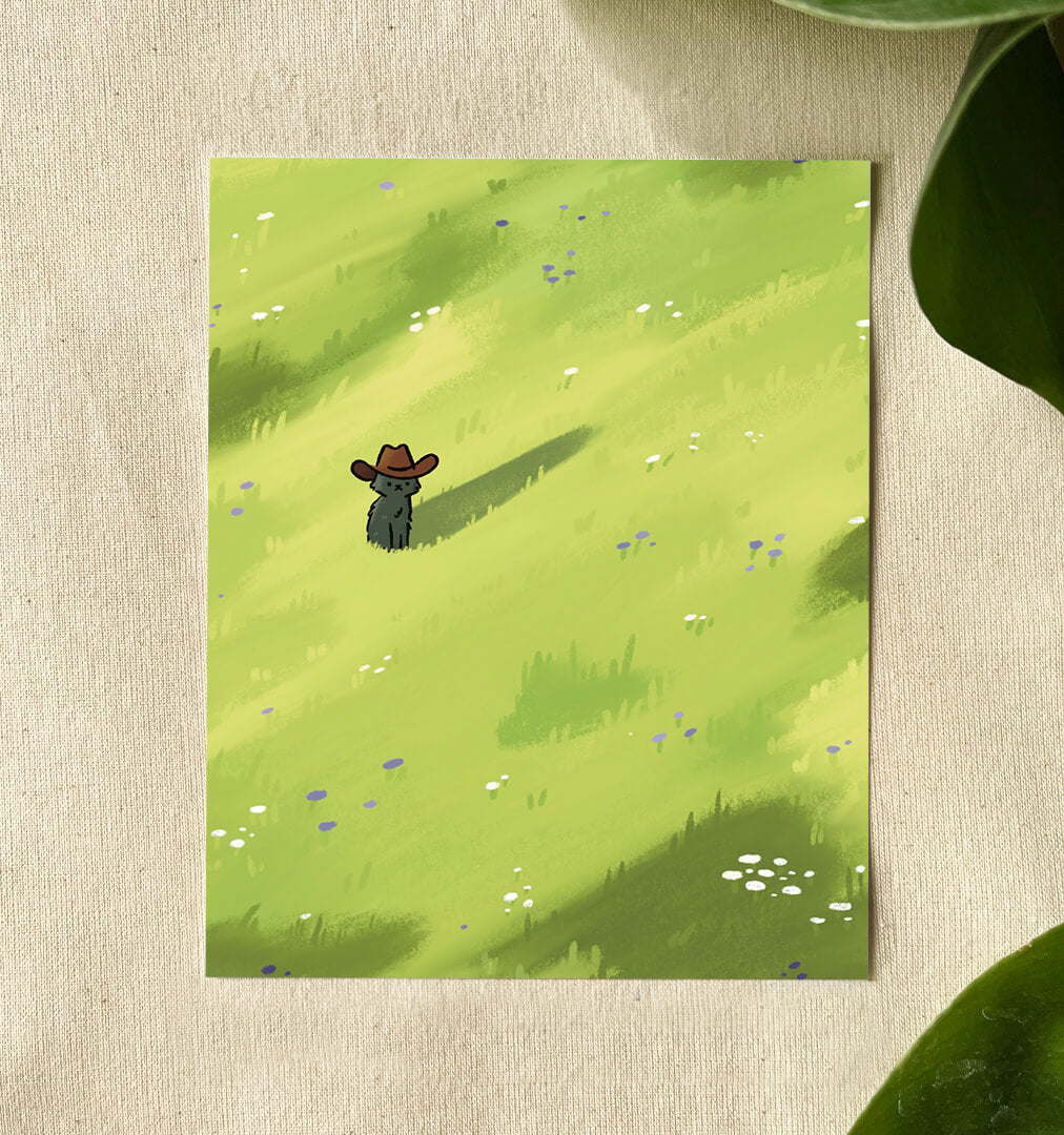 Cowboy cat art print of a cute black cat wearing a cowboy hat stands in a bright green field dotted with purple and white wildflowers. This sits on a canvas background with green leaves.