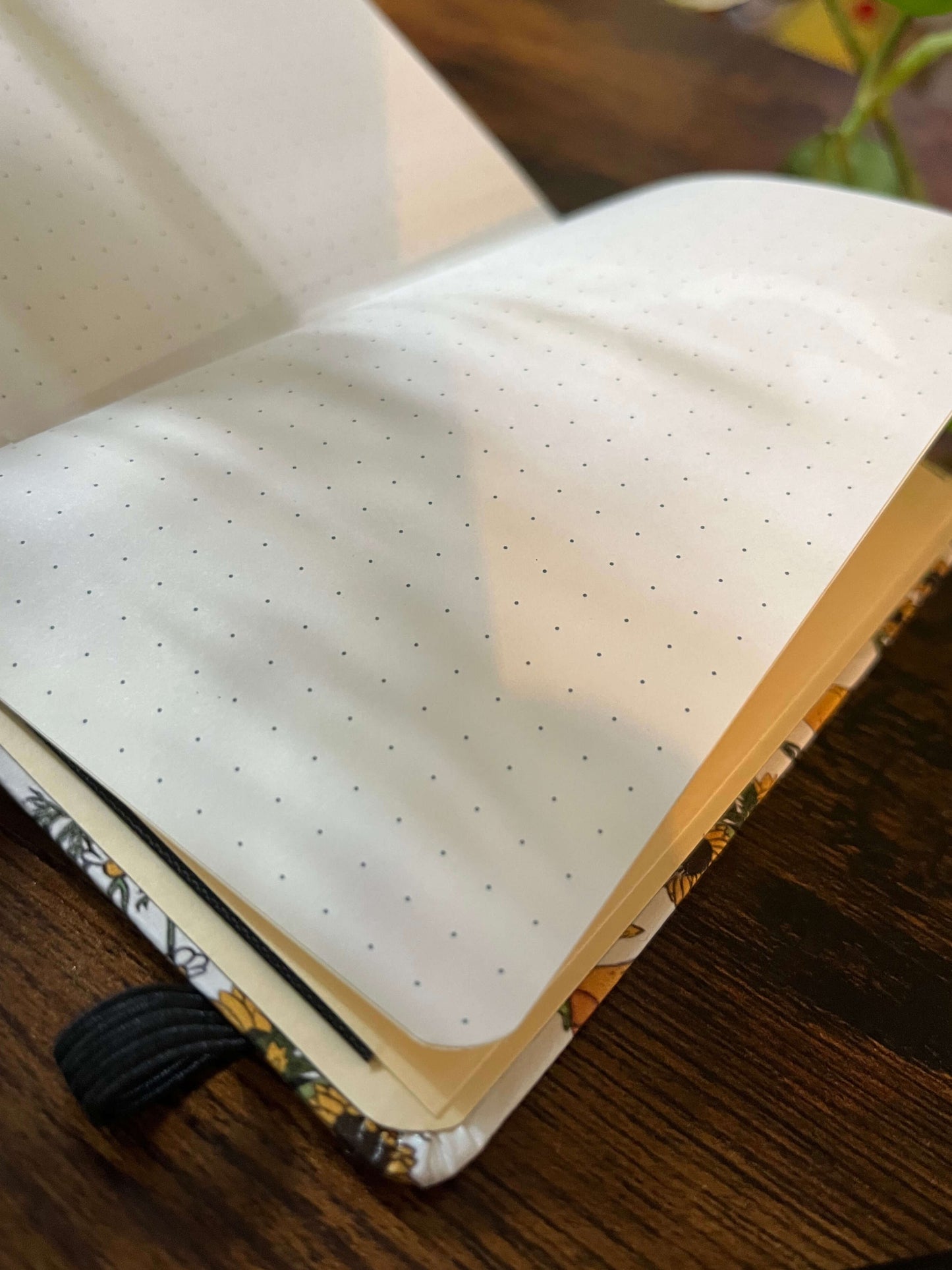 Open dotted notebook on a wooden table, sunlight casting soft leaf shadows on the pages.