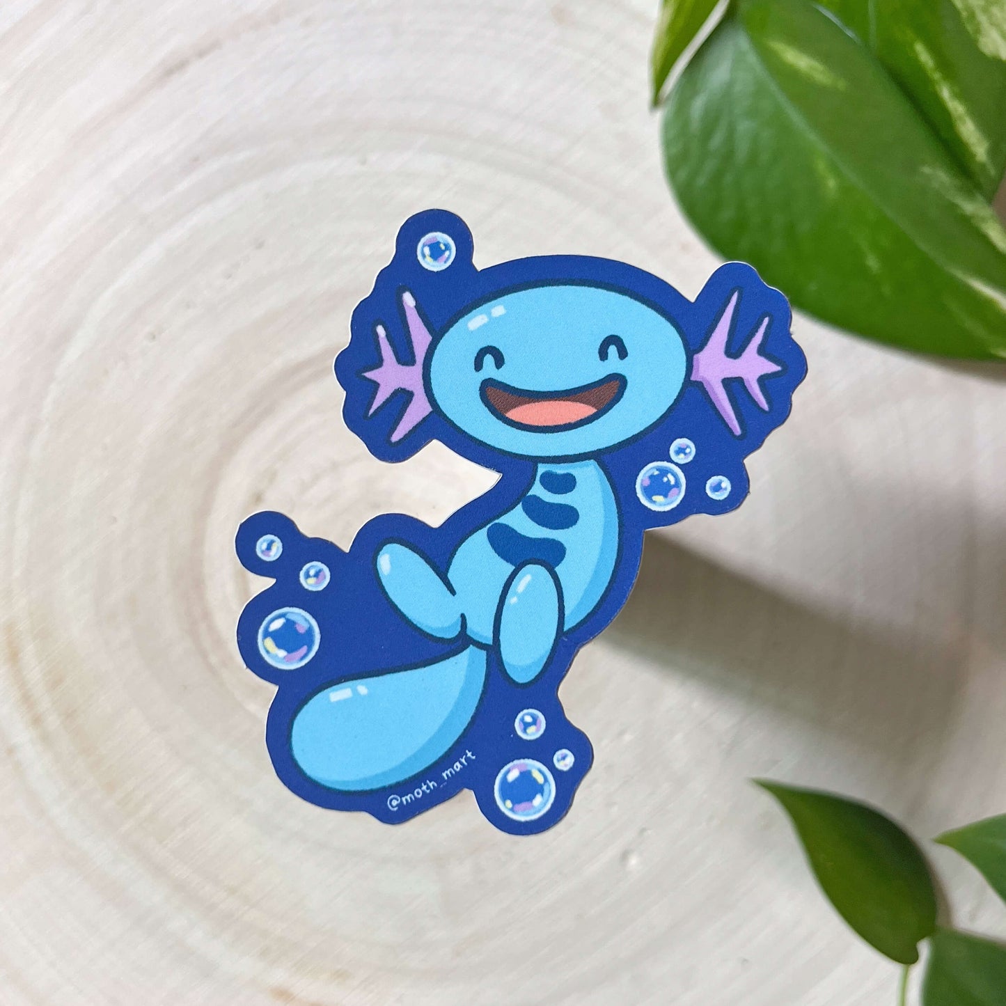 Illustration of a blue axolotl creature with bubbles on a wood back with leaves