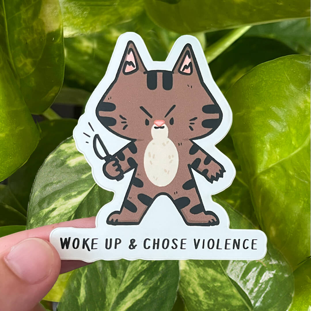 Sticker of a tabby cat holding little knives with the caption "Woke up & Chose Violence".