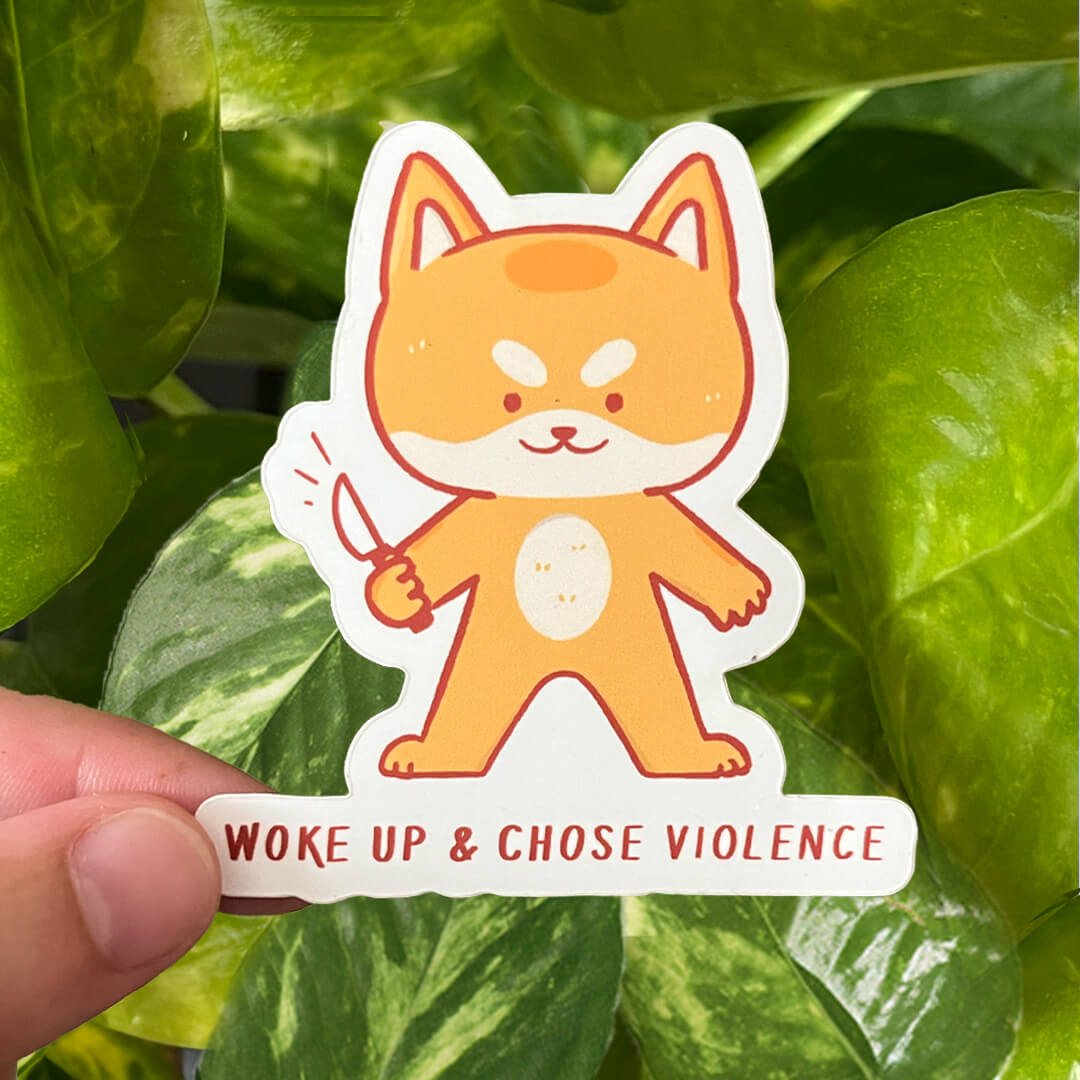 Sticker of yellow shiba dog holding little knives with the caption "Woke up & Chose Violence".