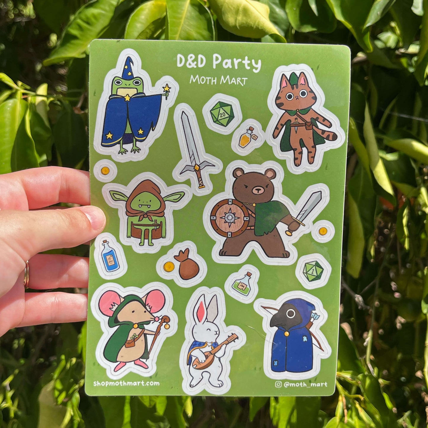 Sticker sheet with various characters and symbols on a green background, held in front of green leaves.