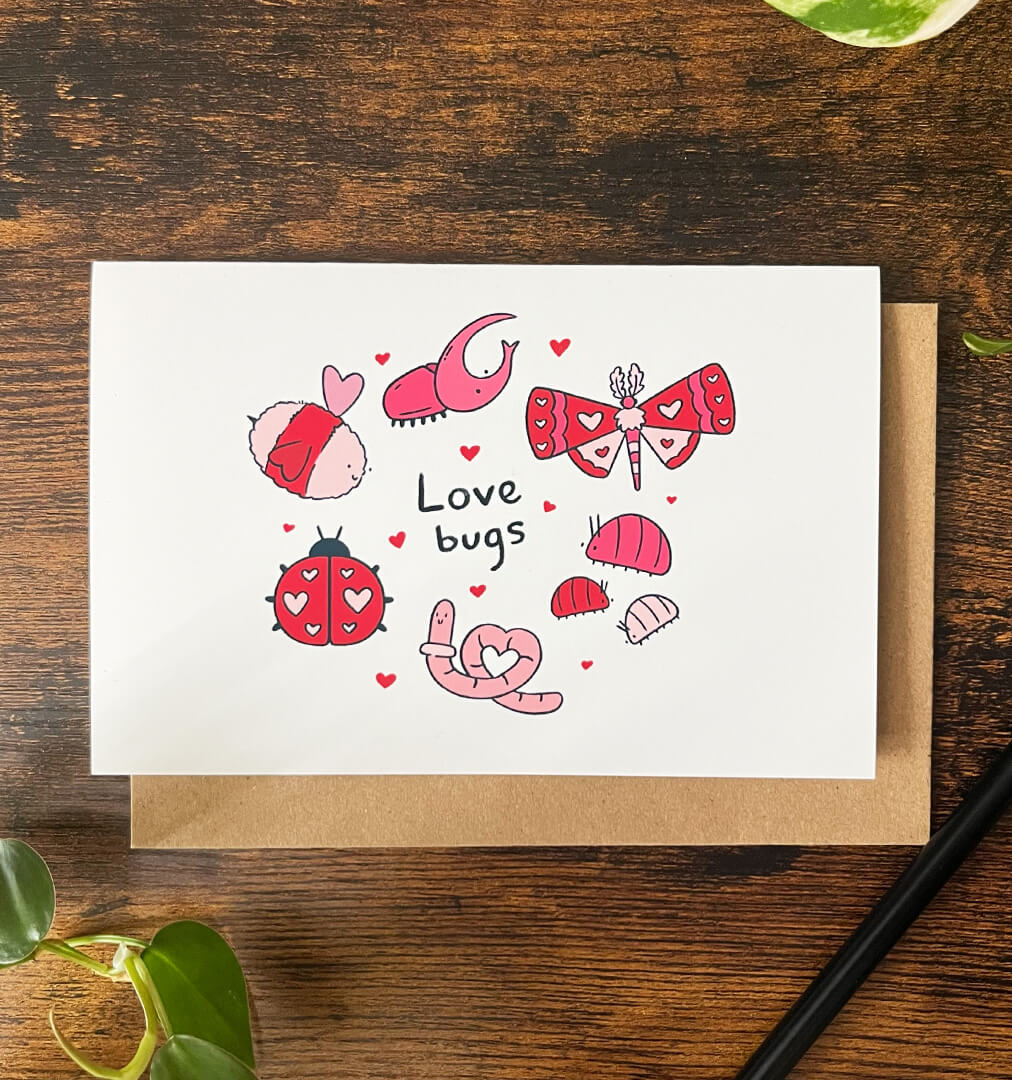Greeting card of 9 red and pink bugs, including a worm, bee, and moth, with the text "love bugs" surrounded by hearts on a wood background.