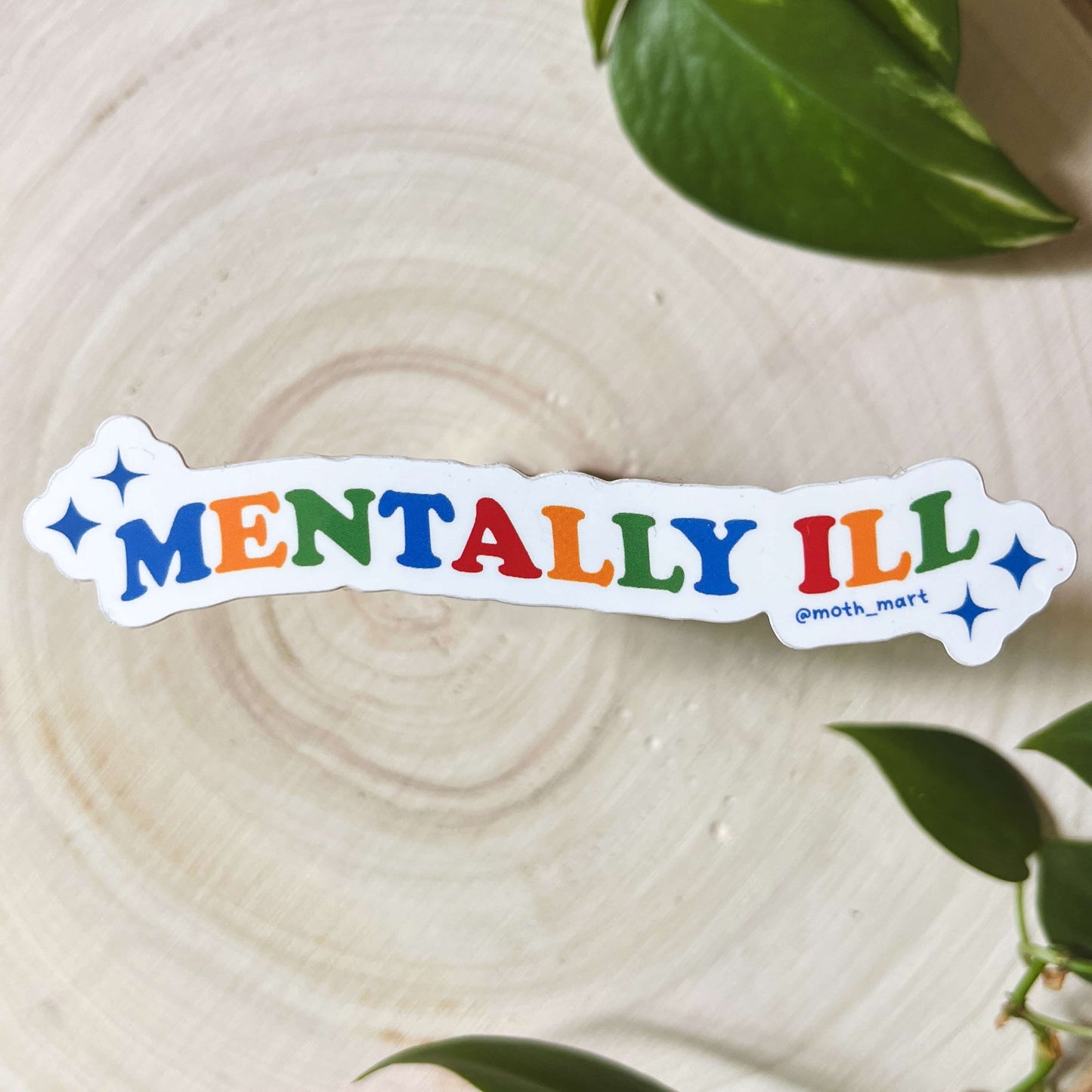 Sticker with the text "Mentally Ill" in primary colors with stars on a wood background with leaves.