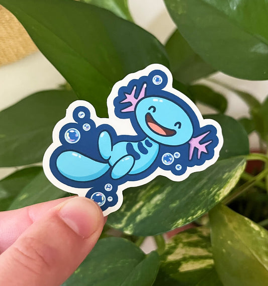 Sticker of blue axolotl Pokemon, Wooper, smiling with bubbles surrounding it. Held by a hand in front of plants.