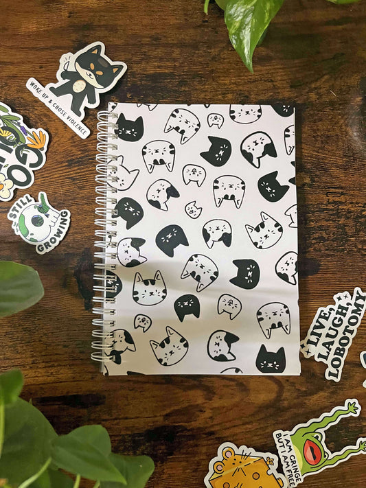 A5 Reusable Cat Sticker book depicting black and white cartoon cat heads. There are 6 stickers surrounding the book.