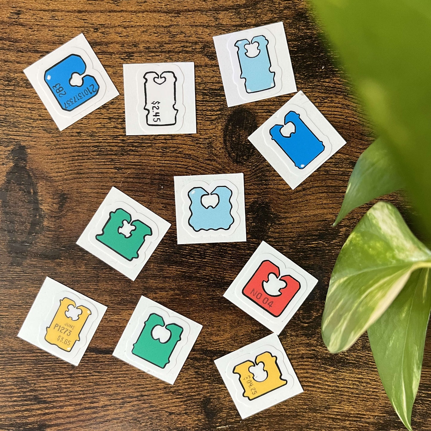 10 colorful, die-cut, bread clip stickers scattered on a wood background with leaves in the corner
