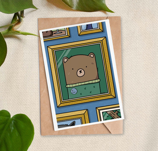 Greeting card with image of framed cartoon of a brown bear wearing a green sweater labeled "Best Bear" on a blue wall.