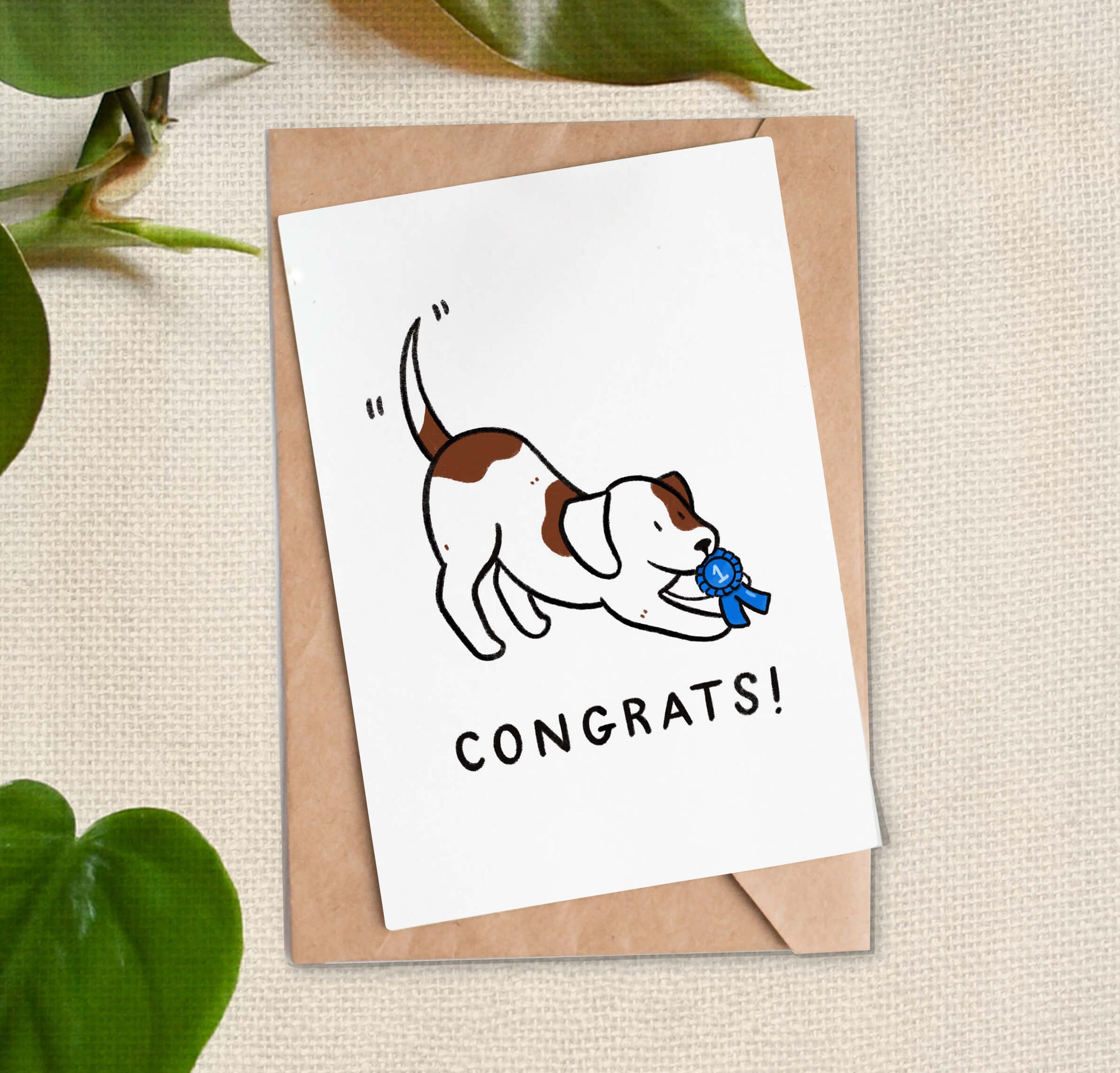 Greeting card with cartoon of a brown and white dog crouching and holding a #1 blue ribbon over "Congrats!" text. 