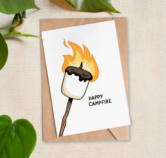 Illustration of a marshmallow with caught flame and burning on a stick with the text "Happy Campfire". 