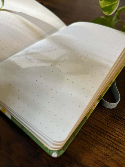 Open dotted notebook on a wooden table, sunlight casting soft leaf shadows on the pages.