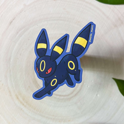 Dark-type cartoon character pocket monster sticker on a textured surface with leaves in the background