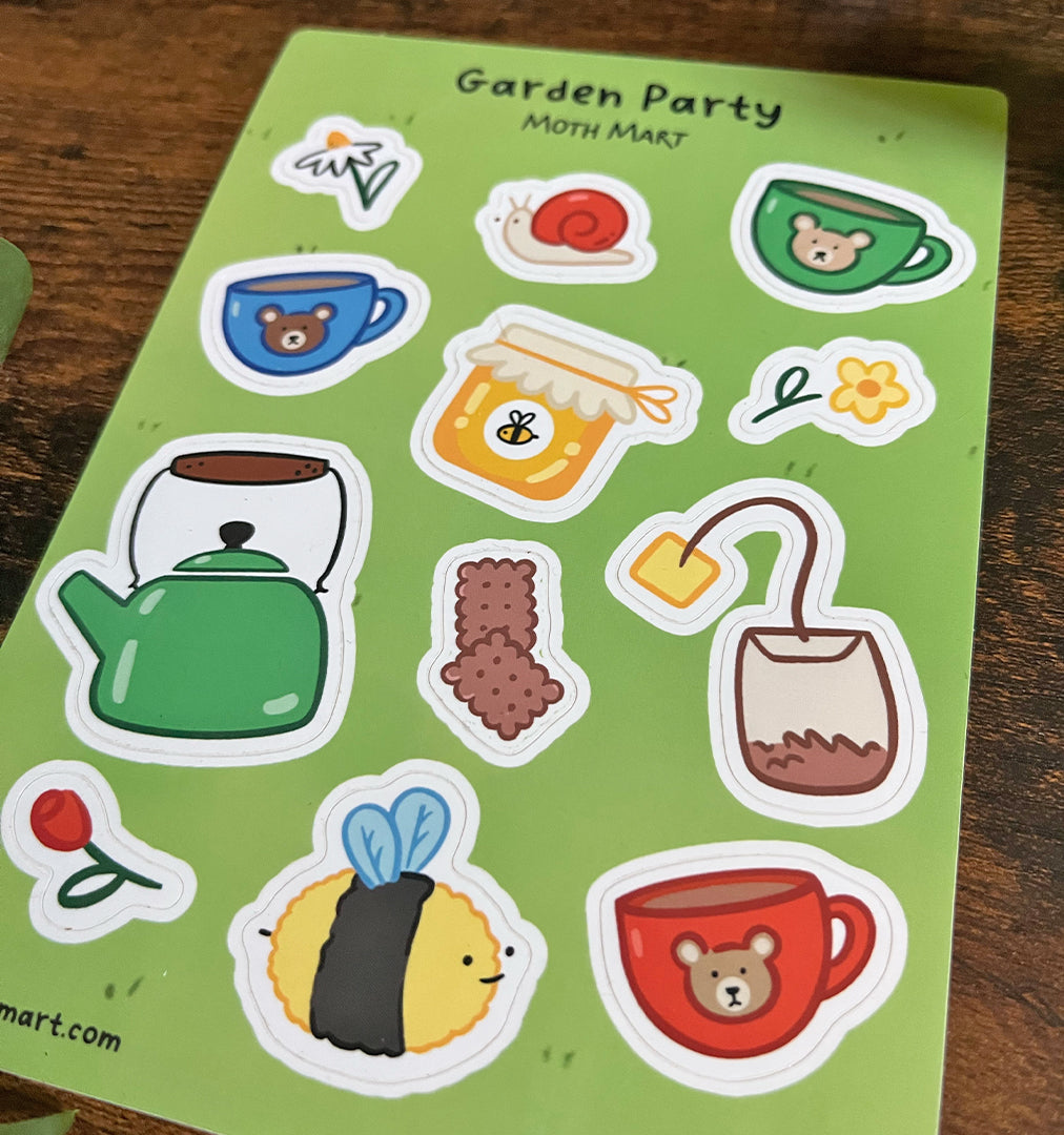 Angled sticker sheet titled "Garden Party" on a grass background. Includes drawings of tea cups, a teapot, honey jar, bee, snail, and flowers on a wood back.