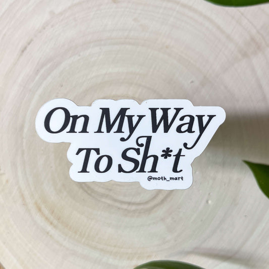 Sticker with text 'On My Way To Sh*t' on a wooden background