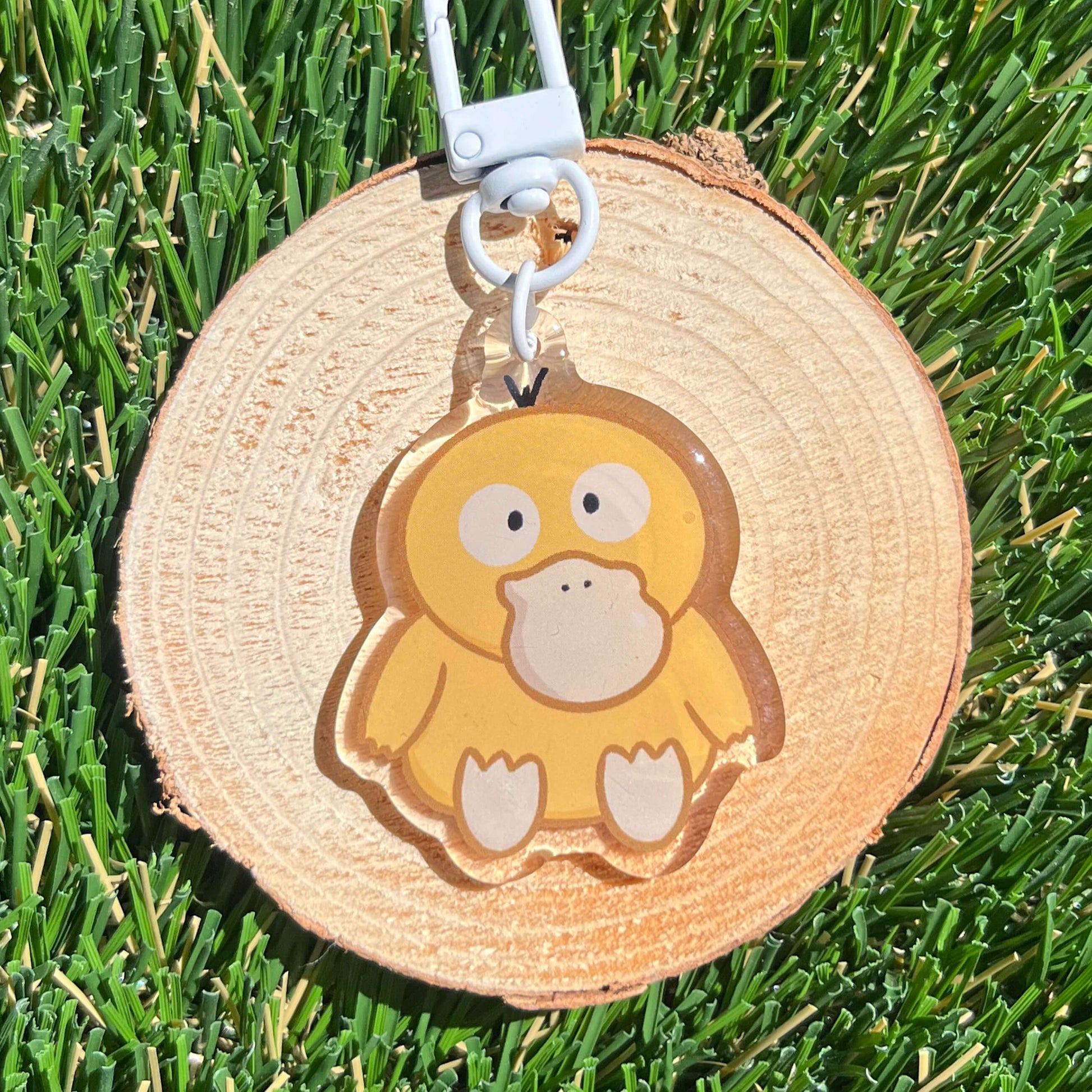 Duck with headache illustration as an acrylic keychain on s wood coaster, set on a grass back