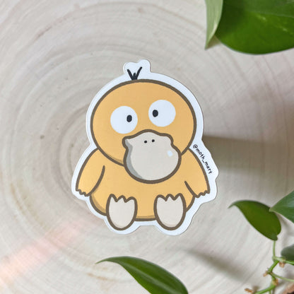 Cartoon yellow duck sticker on a wooden surface with green leaves