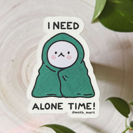 Sticker with cartoon character and text 'I Need Alone Time!' on a wood background with green leaves.
