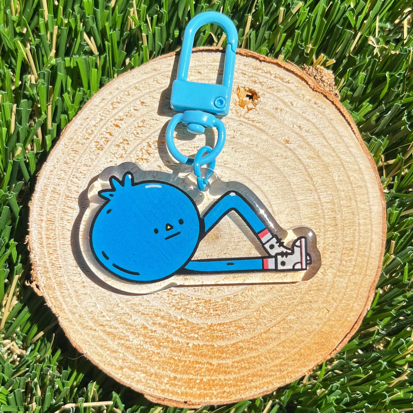 Blue cartoon character keychain on a wooden disc with grass background