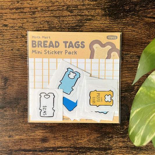 Moth Mart Bread Tags Mini Sticker Pack on a wooden surface with a plant leaf in the corner.