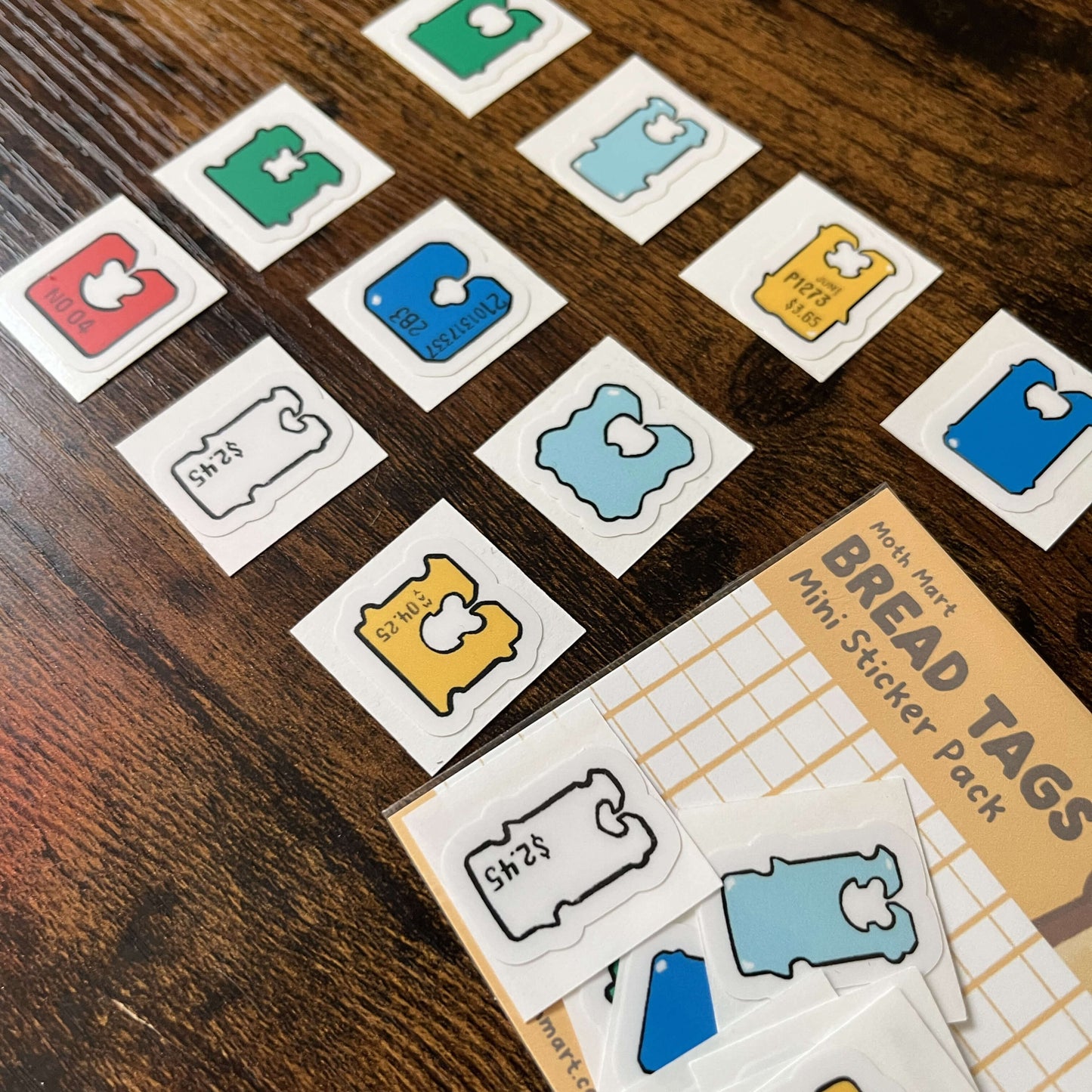 Colorful, die-cut, bread tag stickers on a wooden surface with 'Bread Tags' packaging.