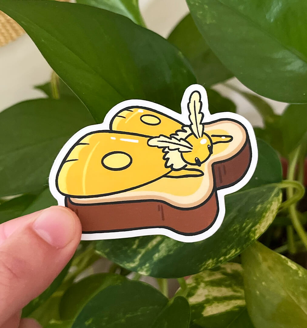 Sticker of a yellow moth laying on top of a piece of toast, melting like butter, held by a hand in front of plants. 