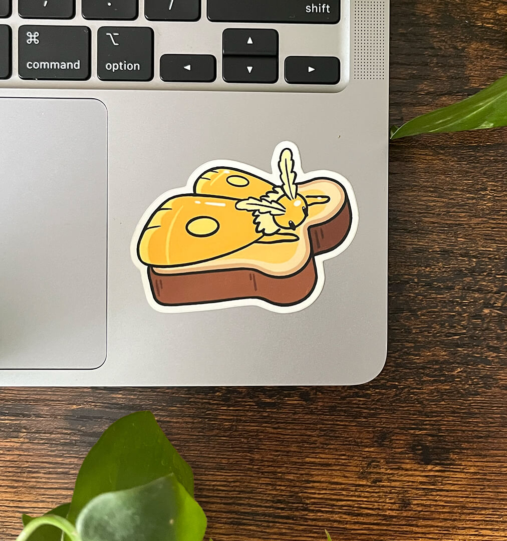 Sticker of a yellow moth laying on top of a piece of toast, melting like butter, on the corner of a laptop. 