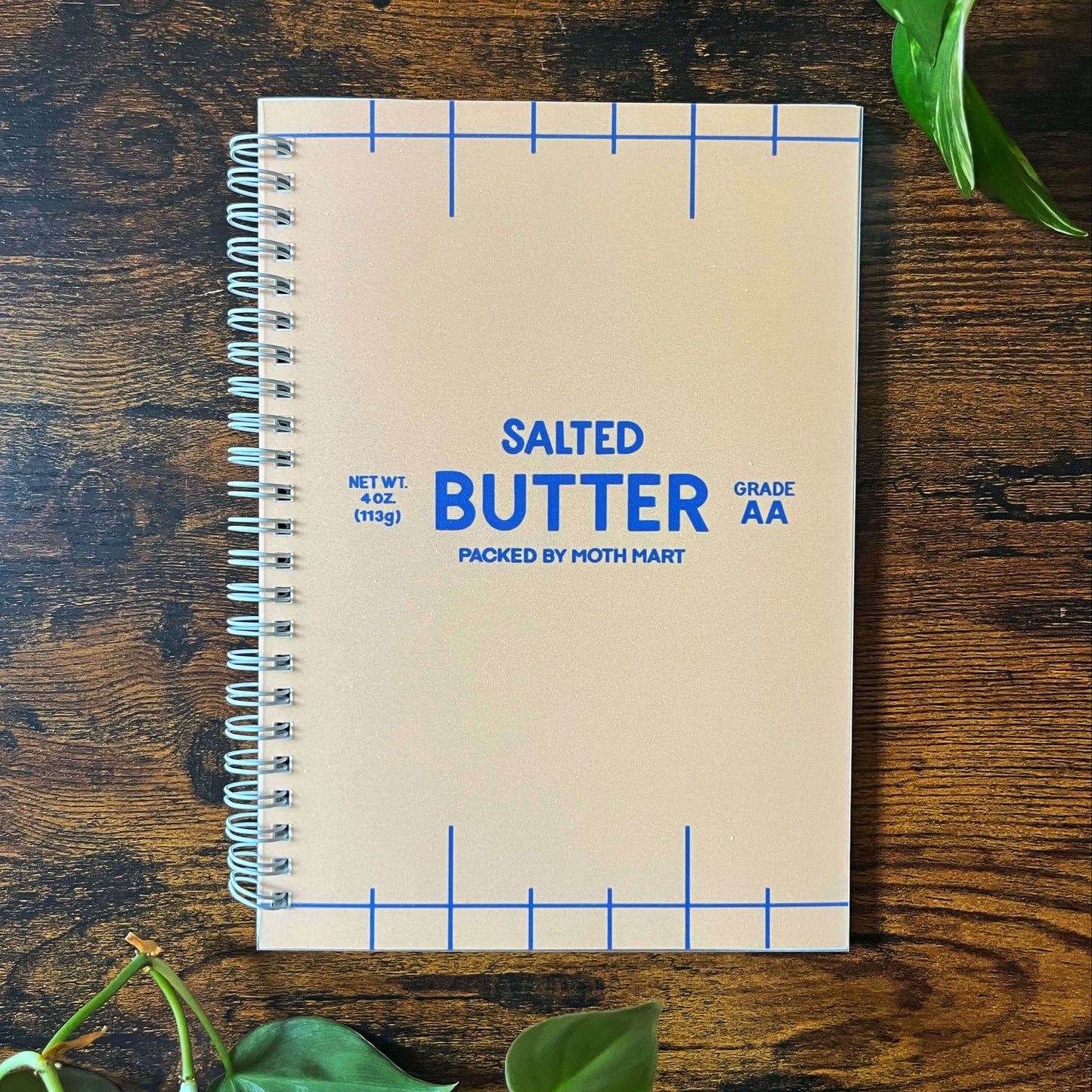 Reusable sticker book with 'Salted Butter' design on a wooden surface with green leaves.