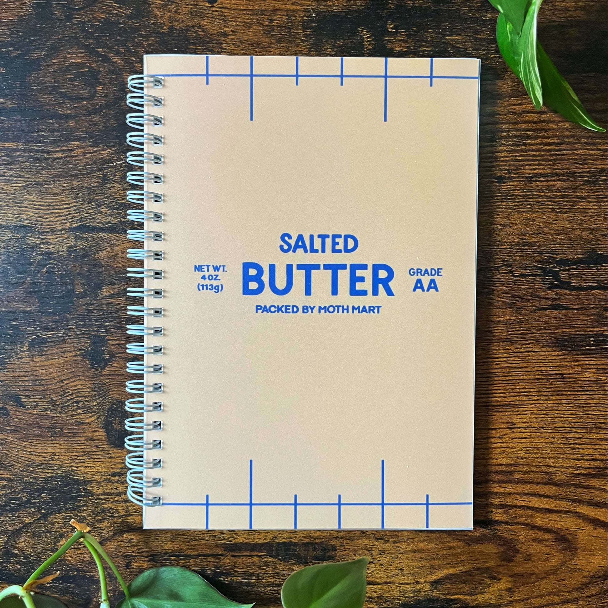 Reusable sticker book with 'Salted Butter' design on a wooden surface with green leaves.