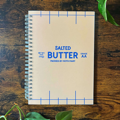 Reusable sticker book with 'Salted Butter' design on a wooden surface with green leaves.