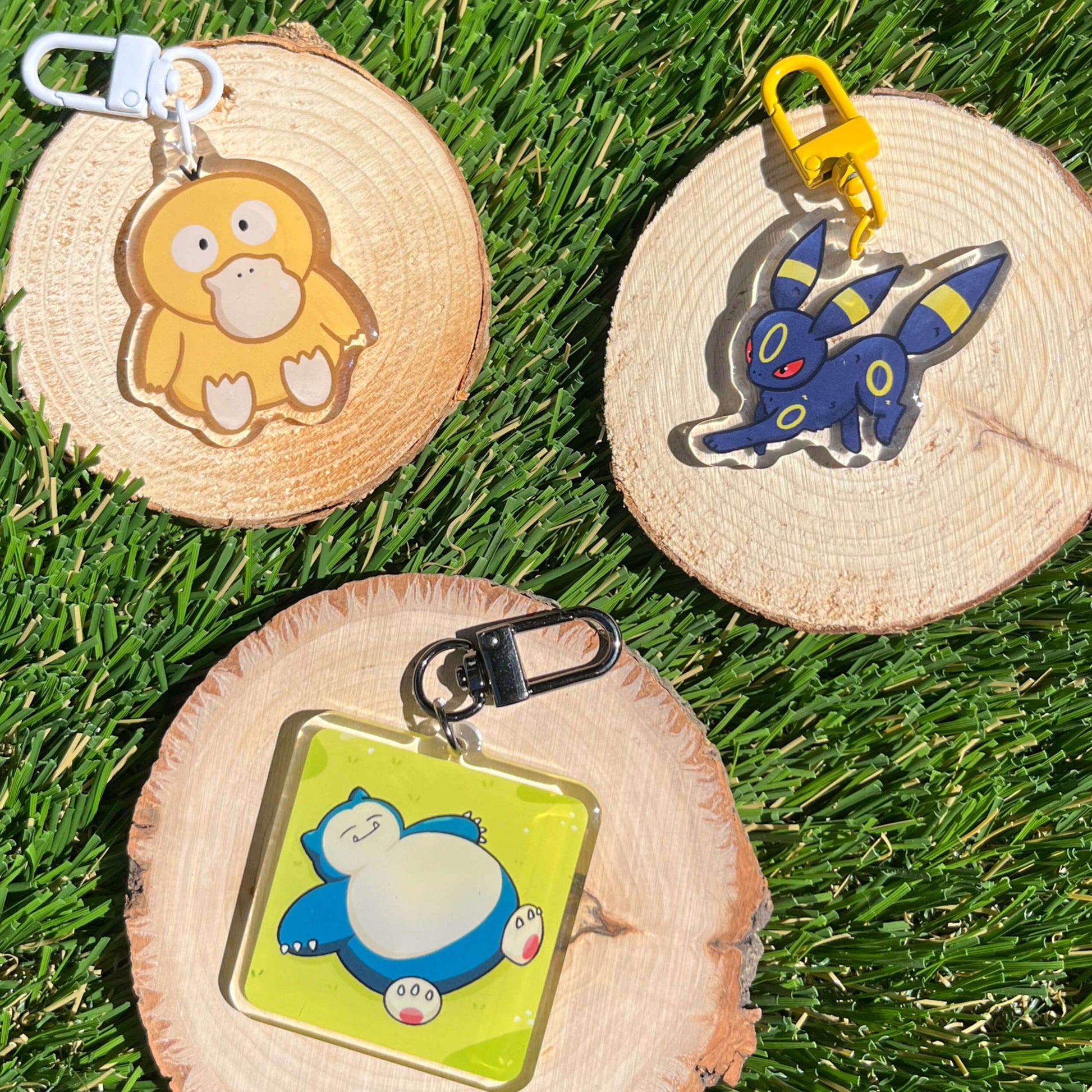 Three cartoon character keychains on wooden slices with grass background