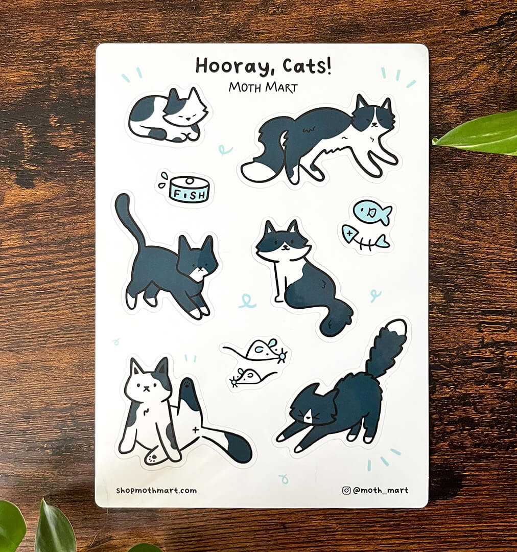 Cute cartoon sticker sheet featuring playful cats, fish, and pet accessories on a wooden table. 