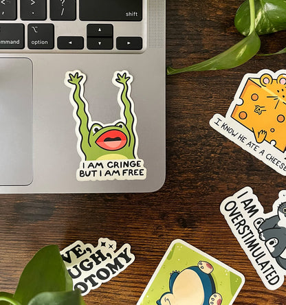 Laptop sticker of a green frog with wavy arms reading "I AM CRINGE BUT I AM FREE" with four stickers surrounding the border.