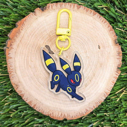 Fox like creature acrylic keychain with yellow clasp on a wood disc, sitting on a grass background.