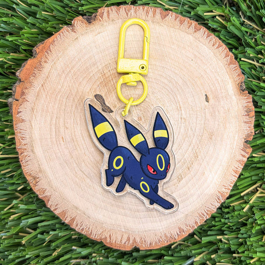 Fox like creature acrylic keychain with yellow clasp on a wood disc, sitting on a grass background.