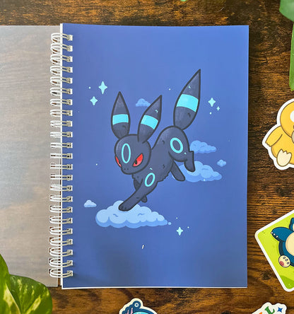 Spiral A5 sticker book featuring a navy blue cat with light blue stripes on clouds surrounded by stars. Open back cover with 4 stickers bordering image. 