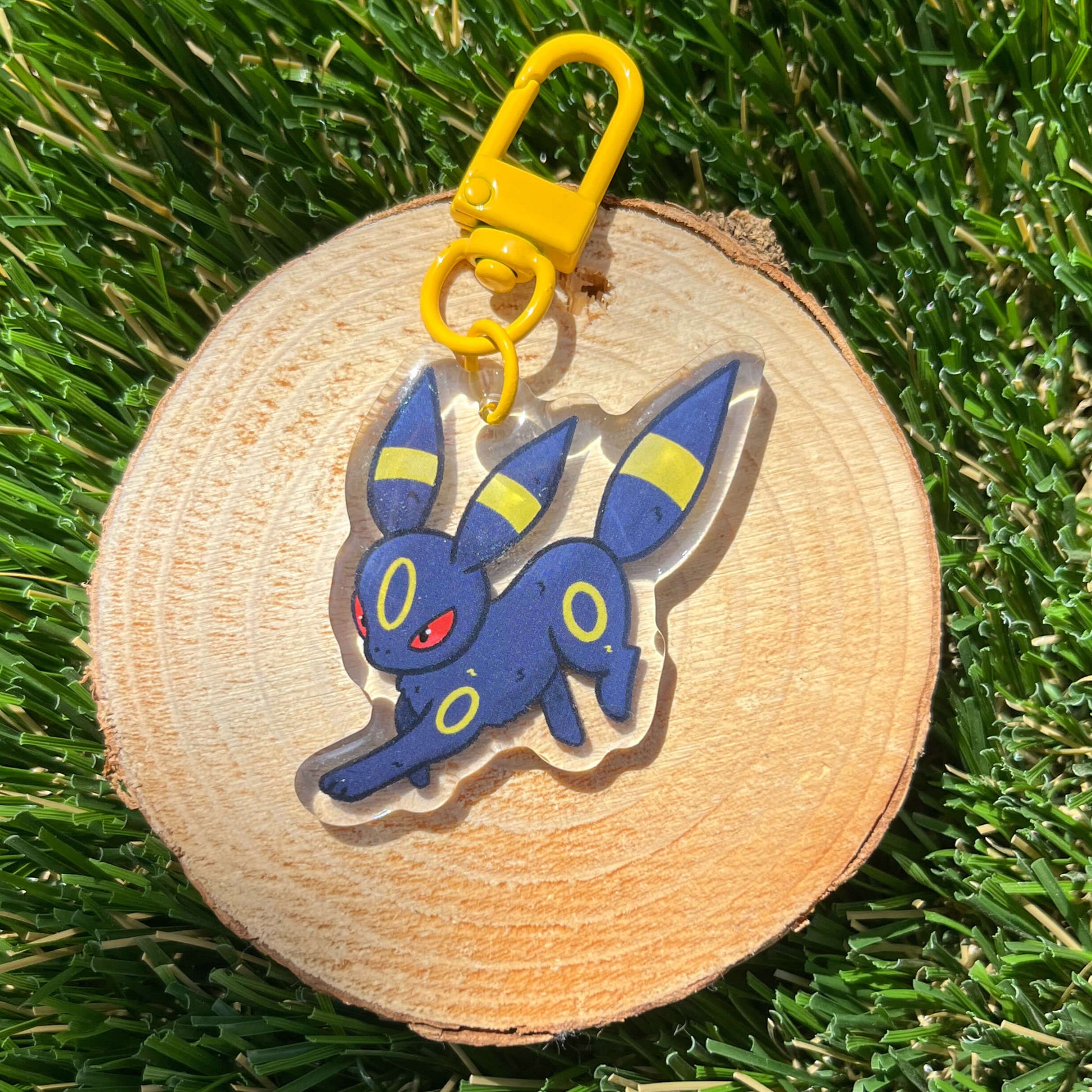 Fox like cartoon character acrylic keychain set on a wood coaster on green grass.