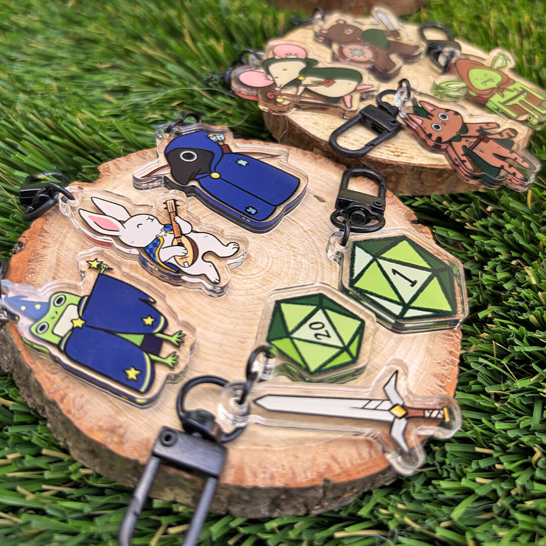 Nine fantasy and gaming-themed animal character acrylic keychains displayed on natural wood slices, displayed on a green grass background. Pictured at an angle. 