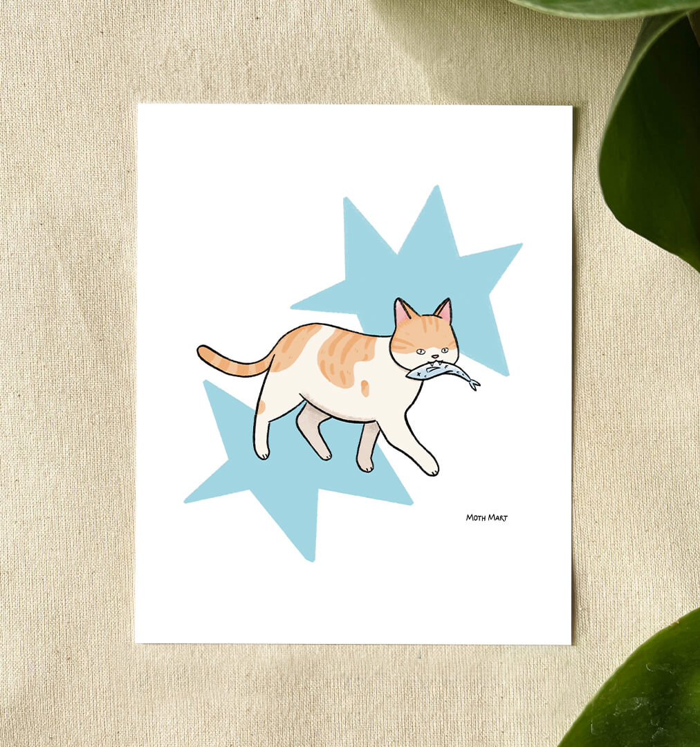 A white art print featuring a cute illustration of an orange and white cat holding a blue fish, set against a light blue star background. The print is displayed on a textured beige surface with green leaves in the corners.