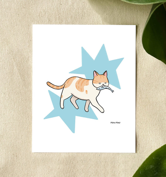 A white art print featuring a cute illustration of an orange and white cat holding a blue fish, set against a light blue star background. The print is displayed on a textured beige surface with green leaves in the corners.