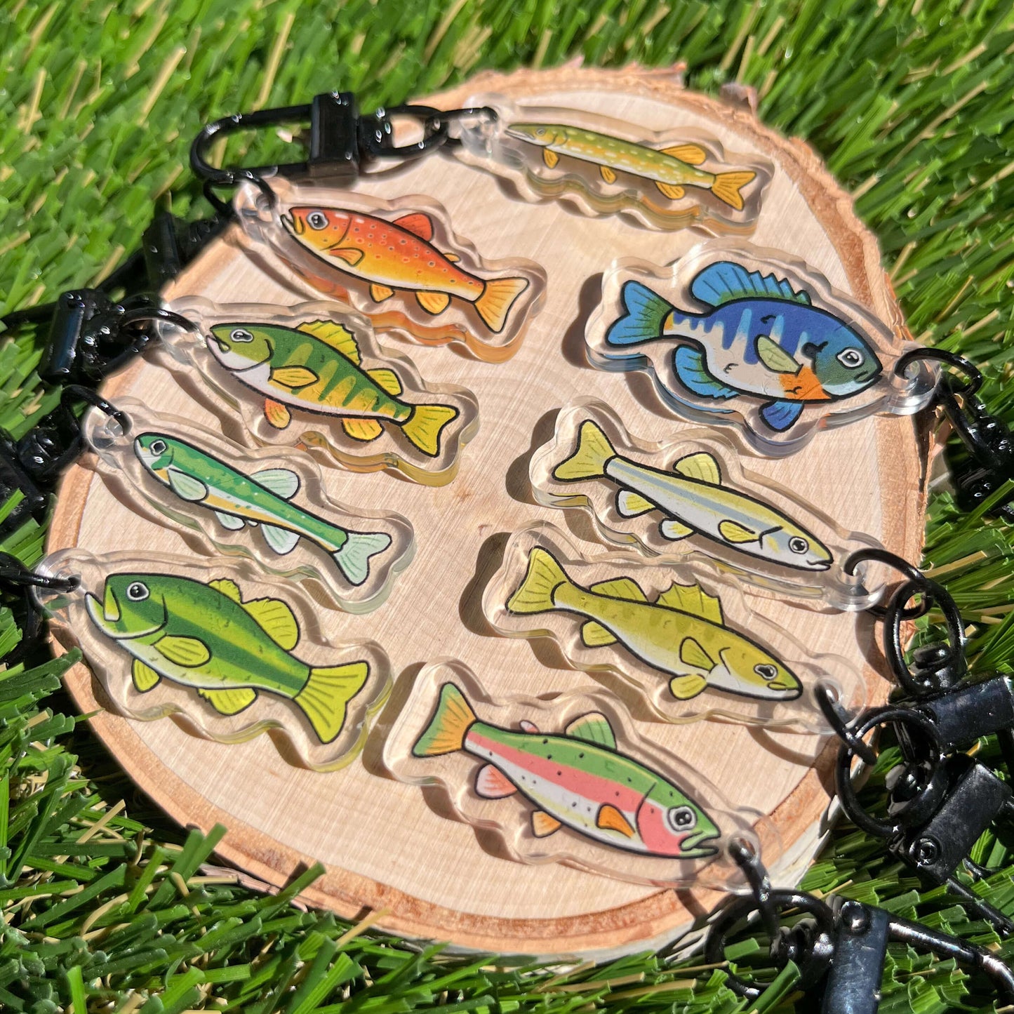 9 bright, acrylic fish keychains sitting on a wood coaster against a grass background.