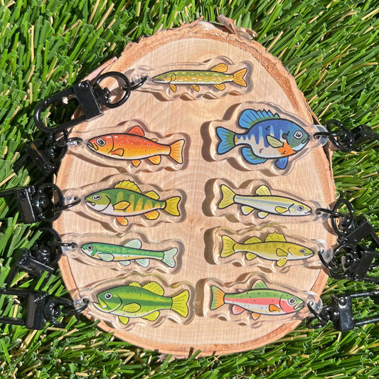 9 fish keychains on a wood coaster set against a grass background