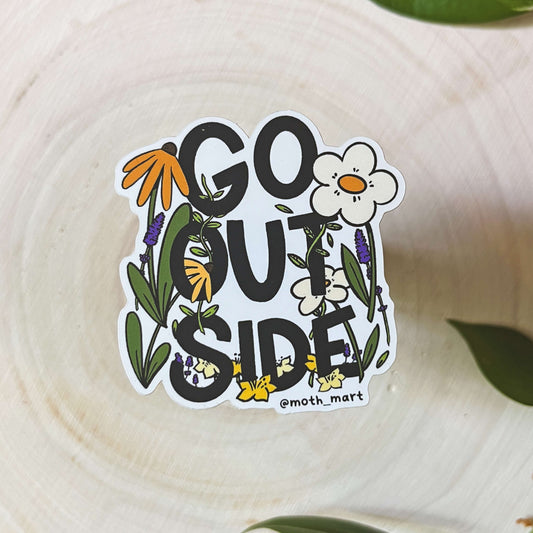 Sticker with 'GO OUTSIDE' text and floral designs on a wooden surface with leaves.