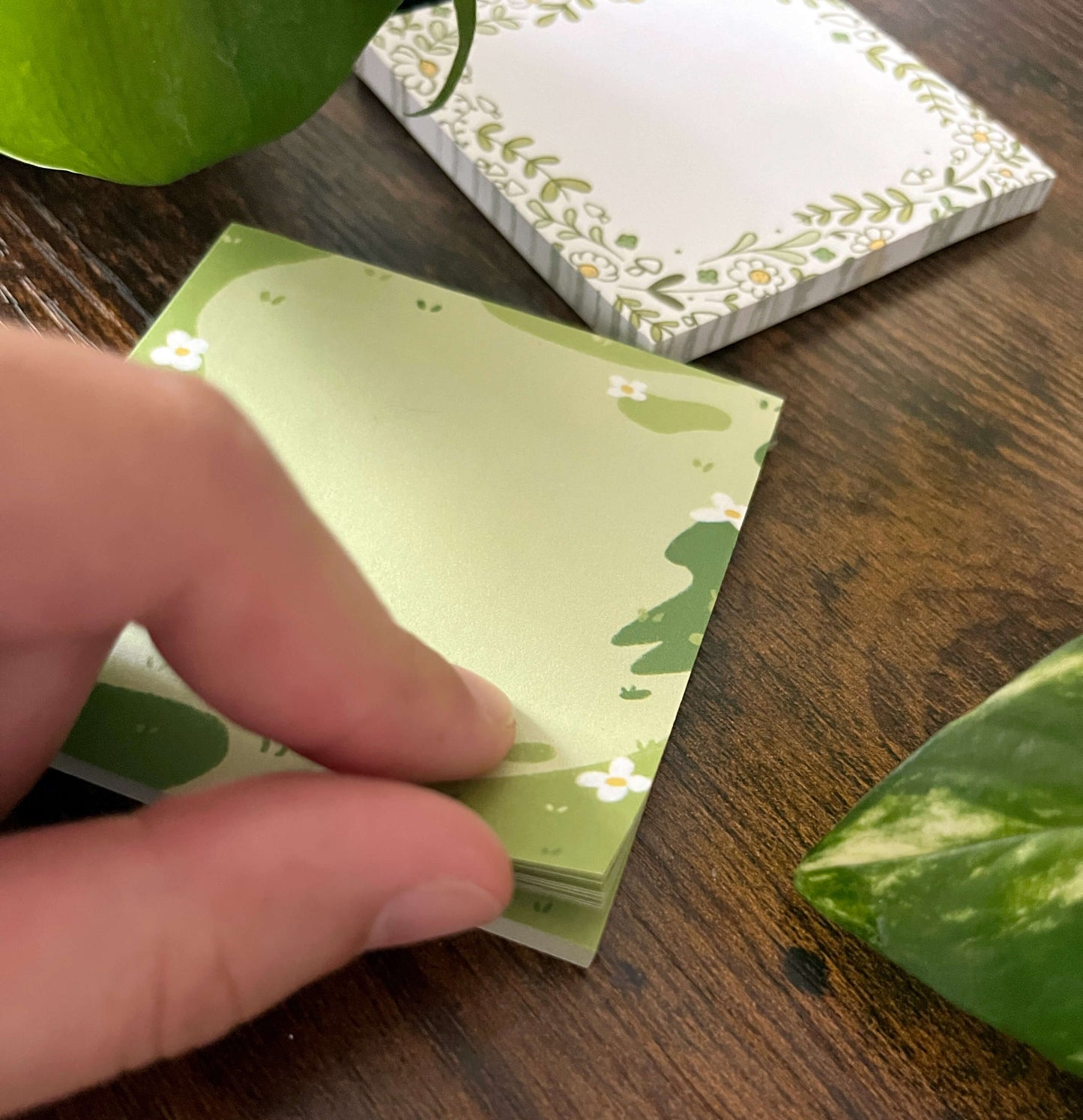 Peeling up the corner of sticky notes that have grass and white flowers. 