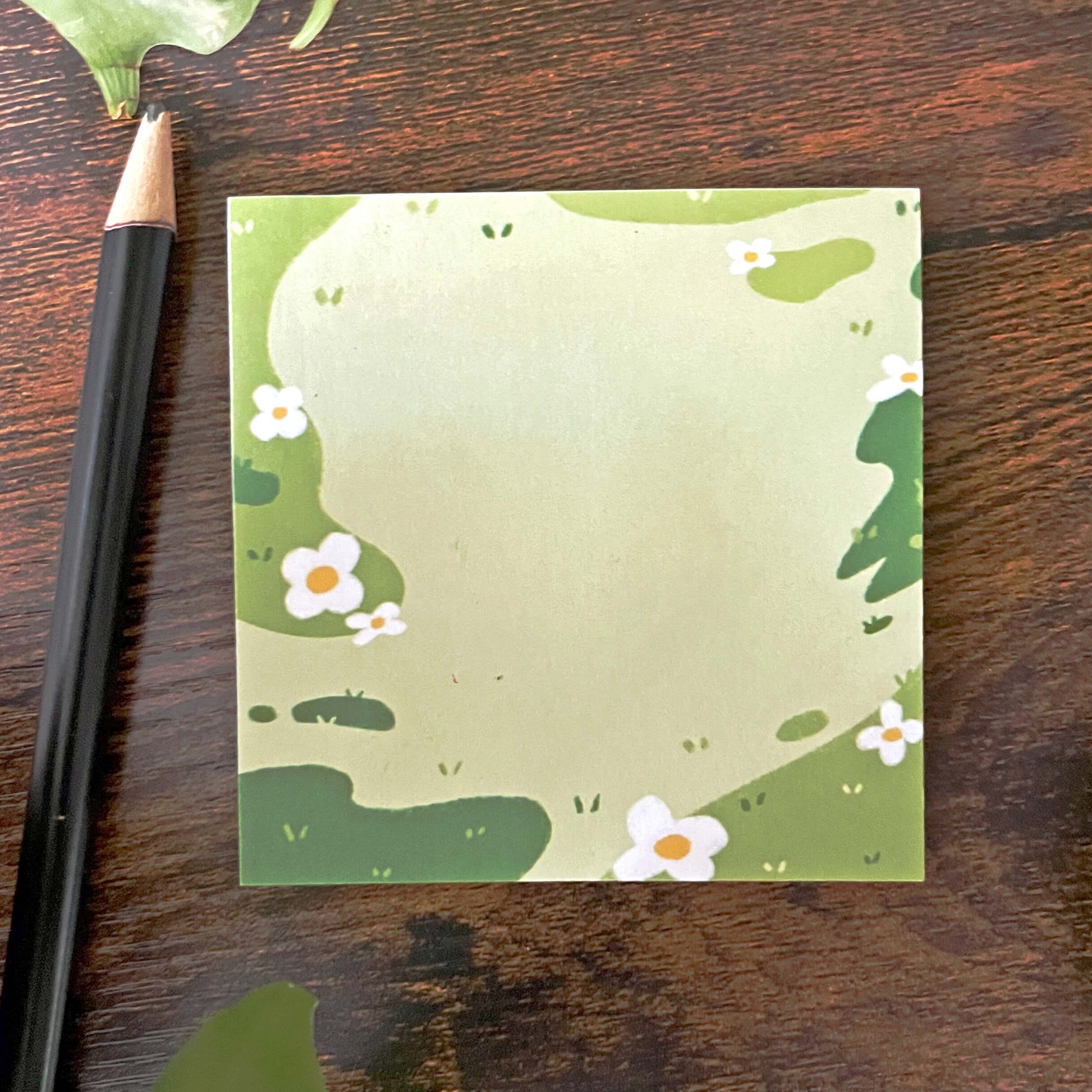 Decorative sticky notes of a grass field with white and yellow flowers. A pencil sits nearby.