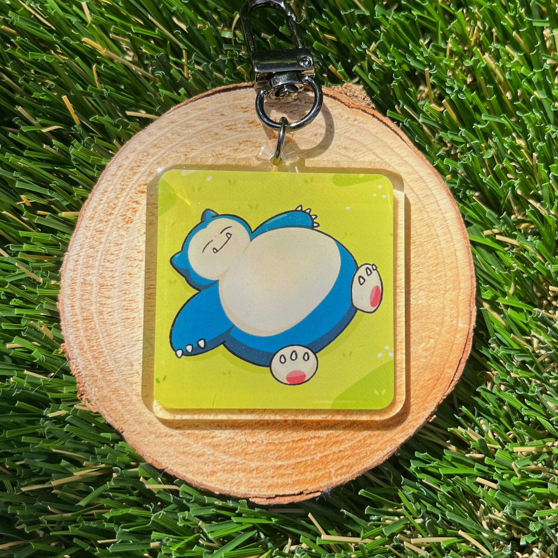 Keychain with blue, sleeping cartoon character on a wooden round base on grass
