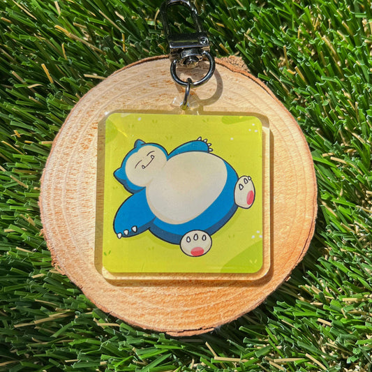 Keychain with blue, sleeping cartoon character on a wooden round base on grass
