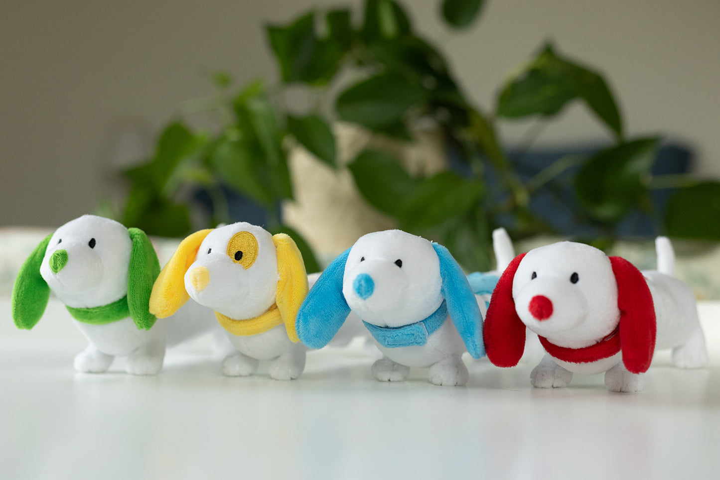 Four colorful dog-shaped toys with different colored collars on a white surface.