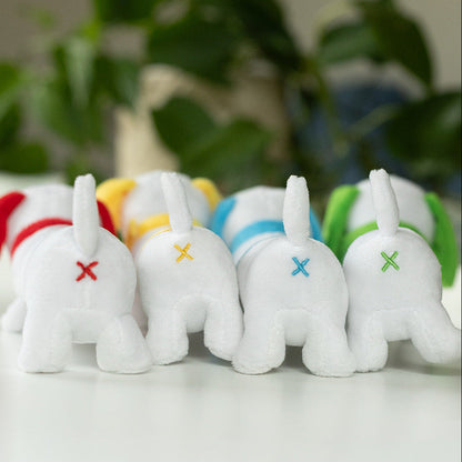 Small white plush toys with colorful crosses on a surface with greenery in the background