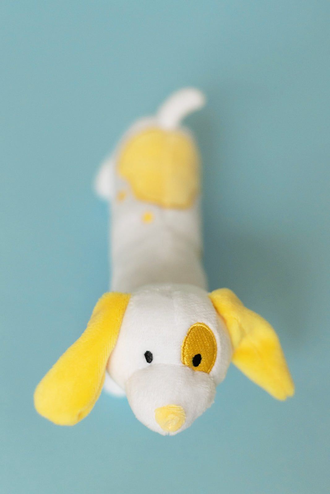 Plush toy resembling a dog with yellow accents on a light blue background