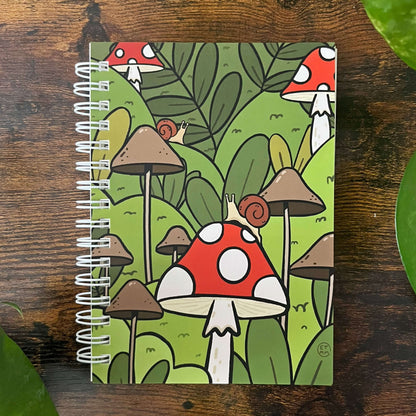 A5 Reusable sticker book with cartoon forest scene with red and white mushrooms, brown mushrooms, and lush green foliage. Two small snails sit on a mushroom.